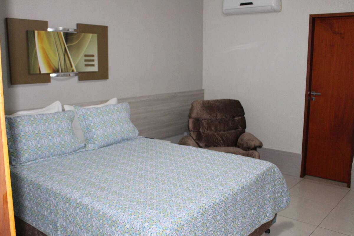 Un dormitorio con cama, una silla, una puerta y aire acondicionado instalado en la pared.