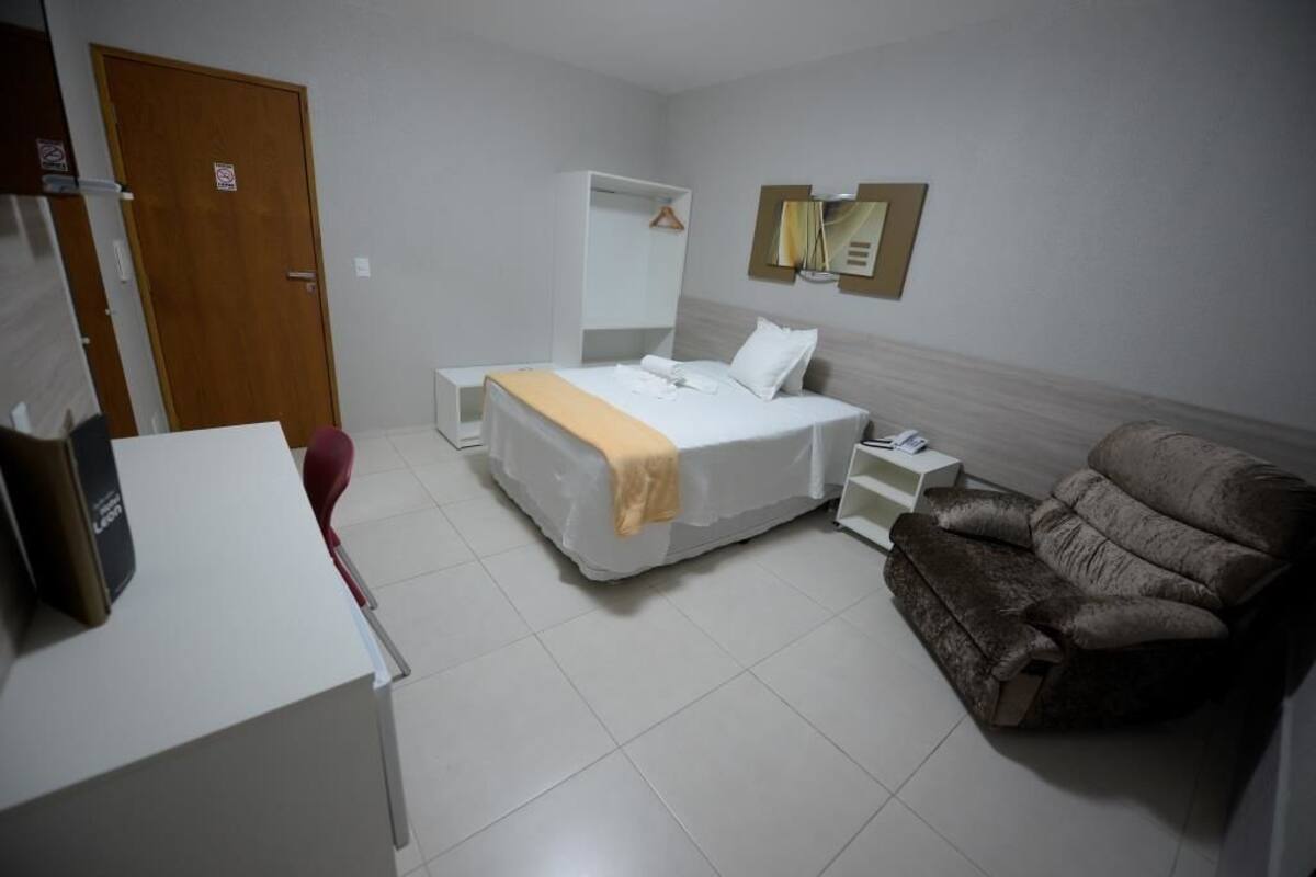 Habitación de hotel con cama, sofá, escritorio, armario y un espejo en la pared.