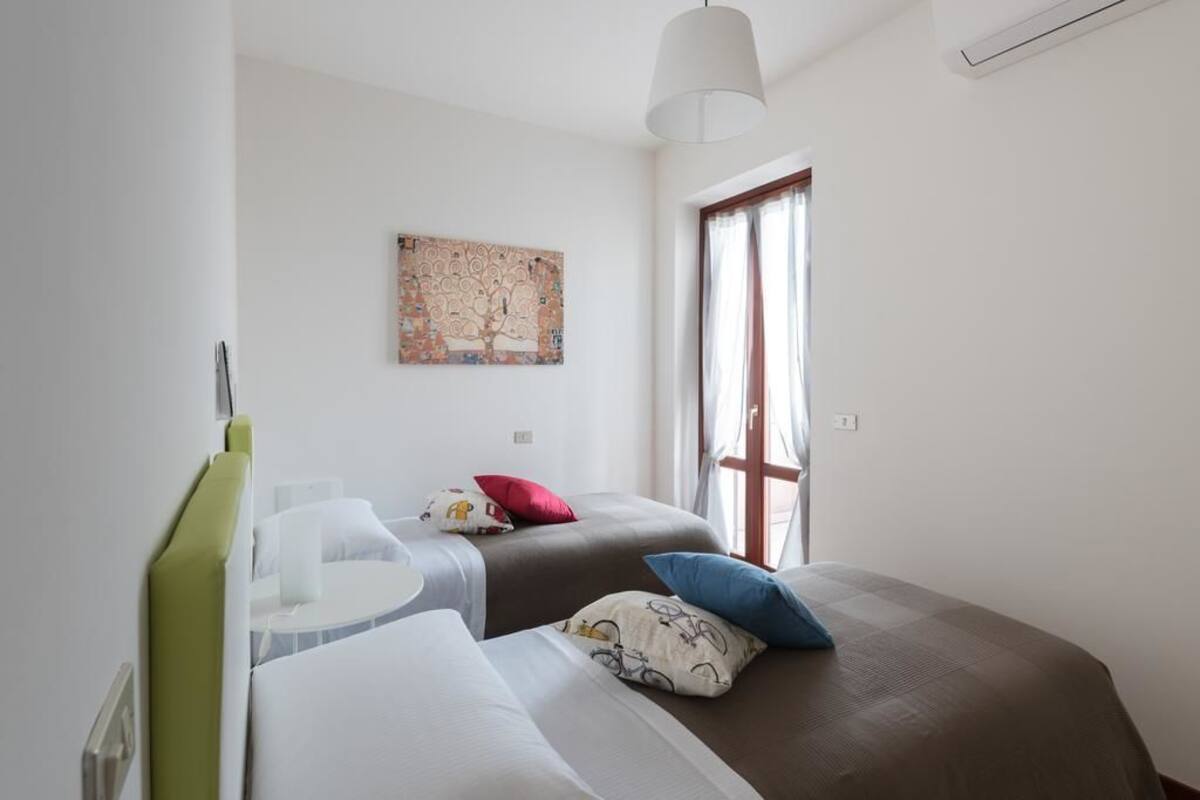 A bedroom with two beds, a window, and a painting on the wall.
