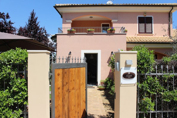 A two-story building with a wooden gate, a balcony with potted plants, and a sign with the name "ELLEBI". - Ellebì B&B (Mosciano Sant'Angelo)
