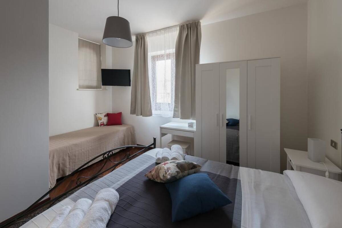 A hotel room with a bed, bedside table, and a desk with a chair.