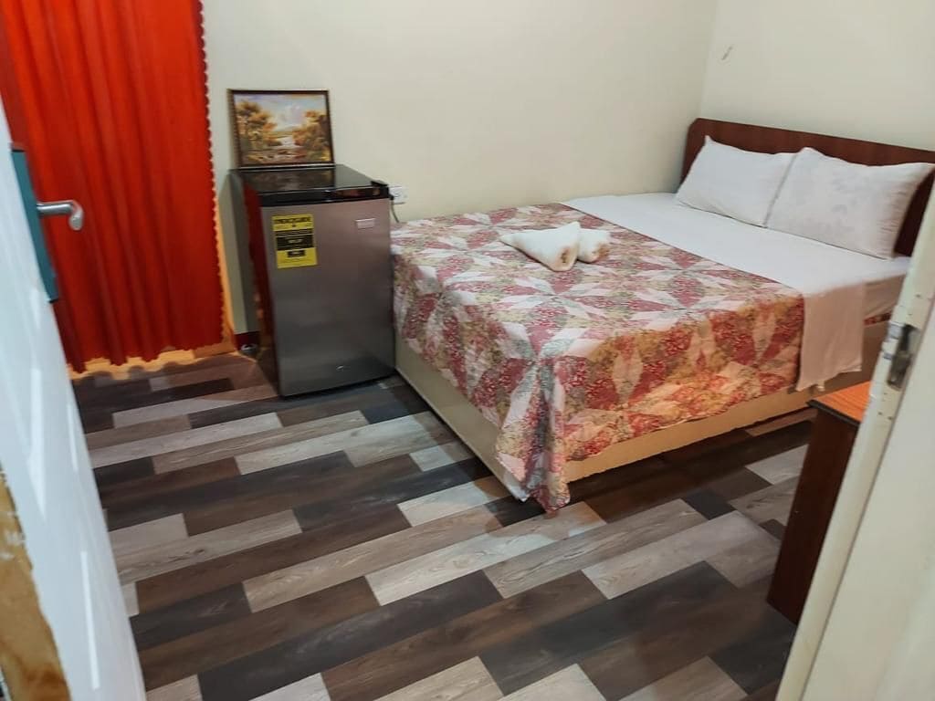 Una habitació amb un llit, un refrigerador petit i una porta amb cortines vermelles.