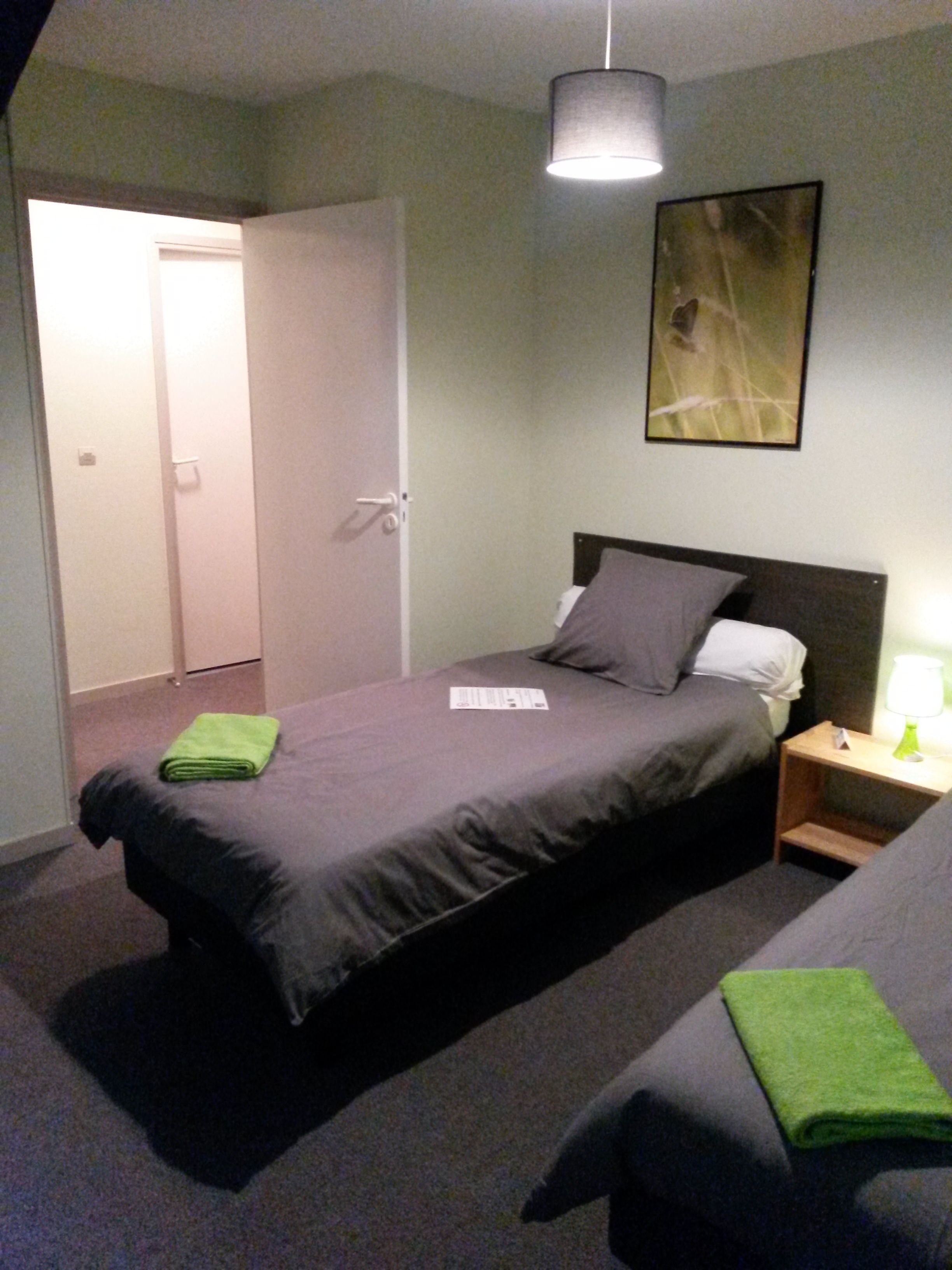 A bedroom with a bed, a nightstand, a green towel, and a painting on the wall.
