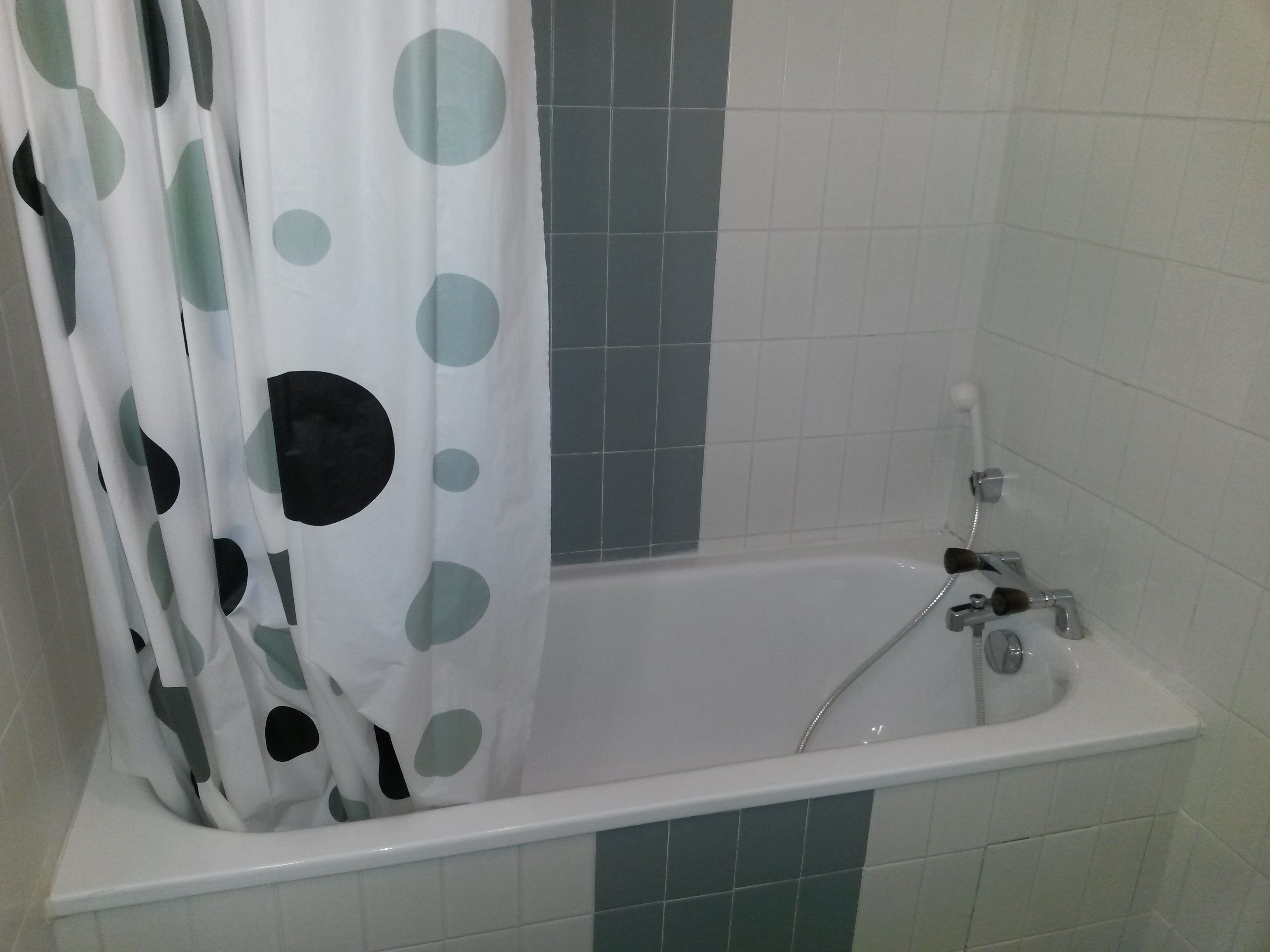 Un baño con bañera, ducha y cortina estampada con lunares.