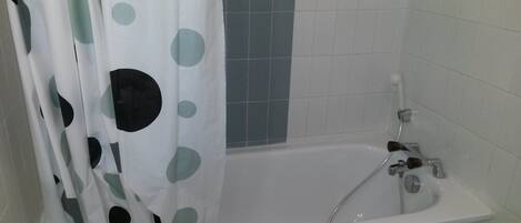 Un baño con bañera, ducha y cortina estampada con lunares.