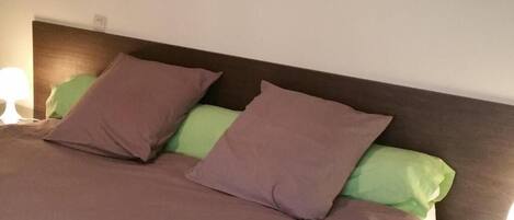 A neatly made bed with a brown bedspread and two pillows, one green and one brown.
