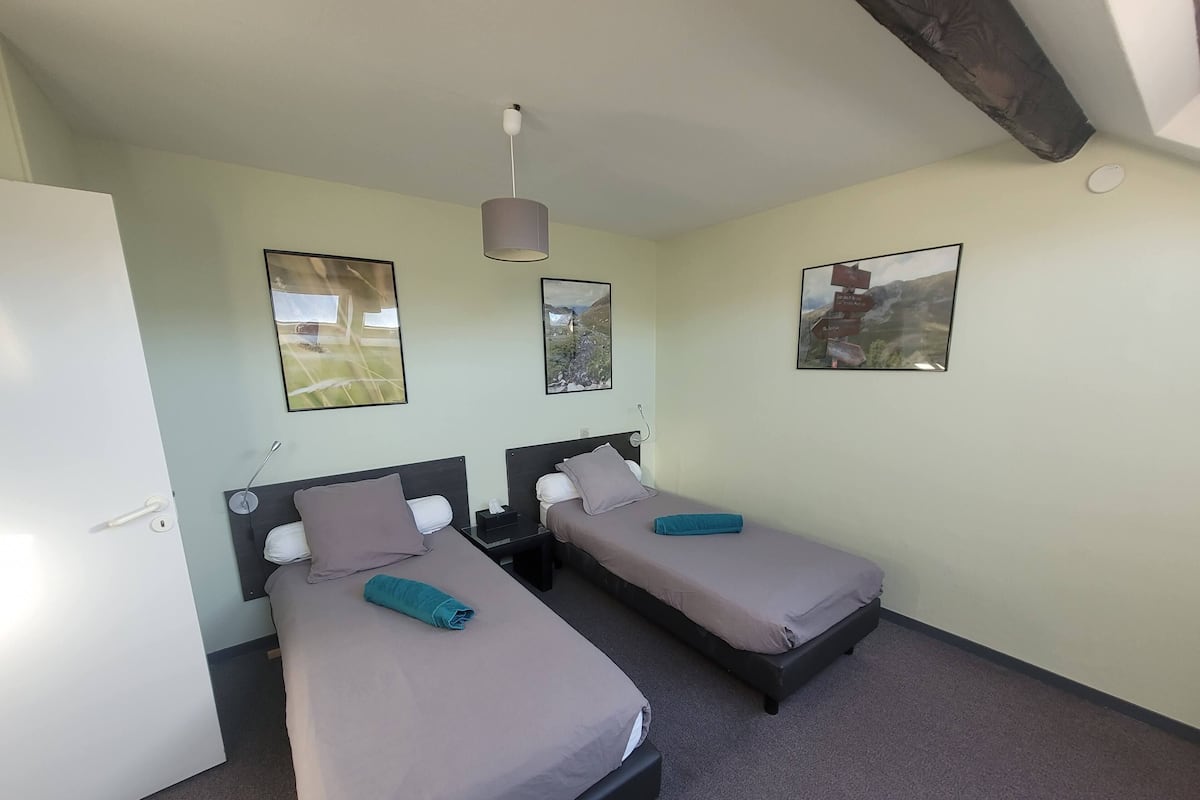 A room with two beds, a door, and three framed pictures on the wall.