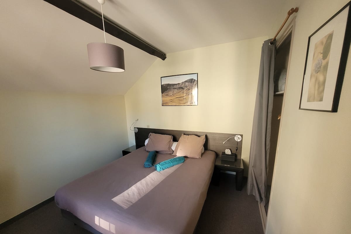A neatly made bed with a headboard, a bedside table with a lamp, and a painting on the wall.