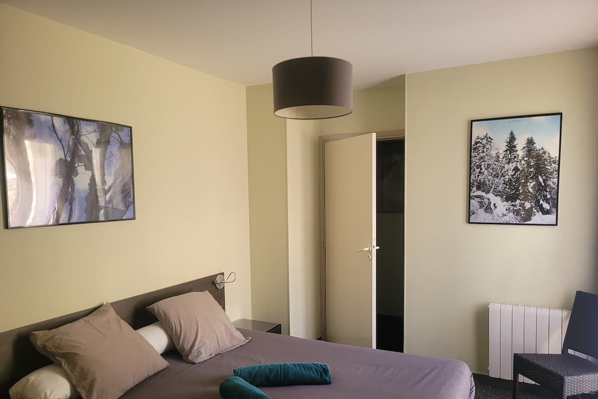A hotel room with a bed, a desk, a chair, and two paintings on the walls.