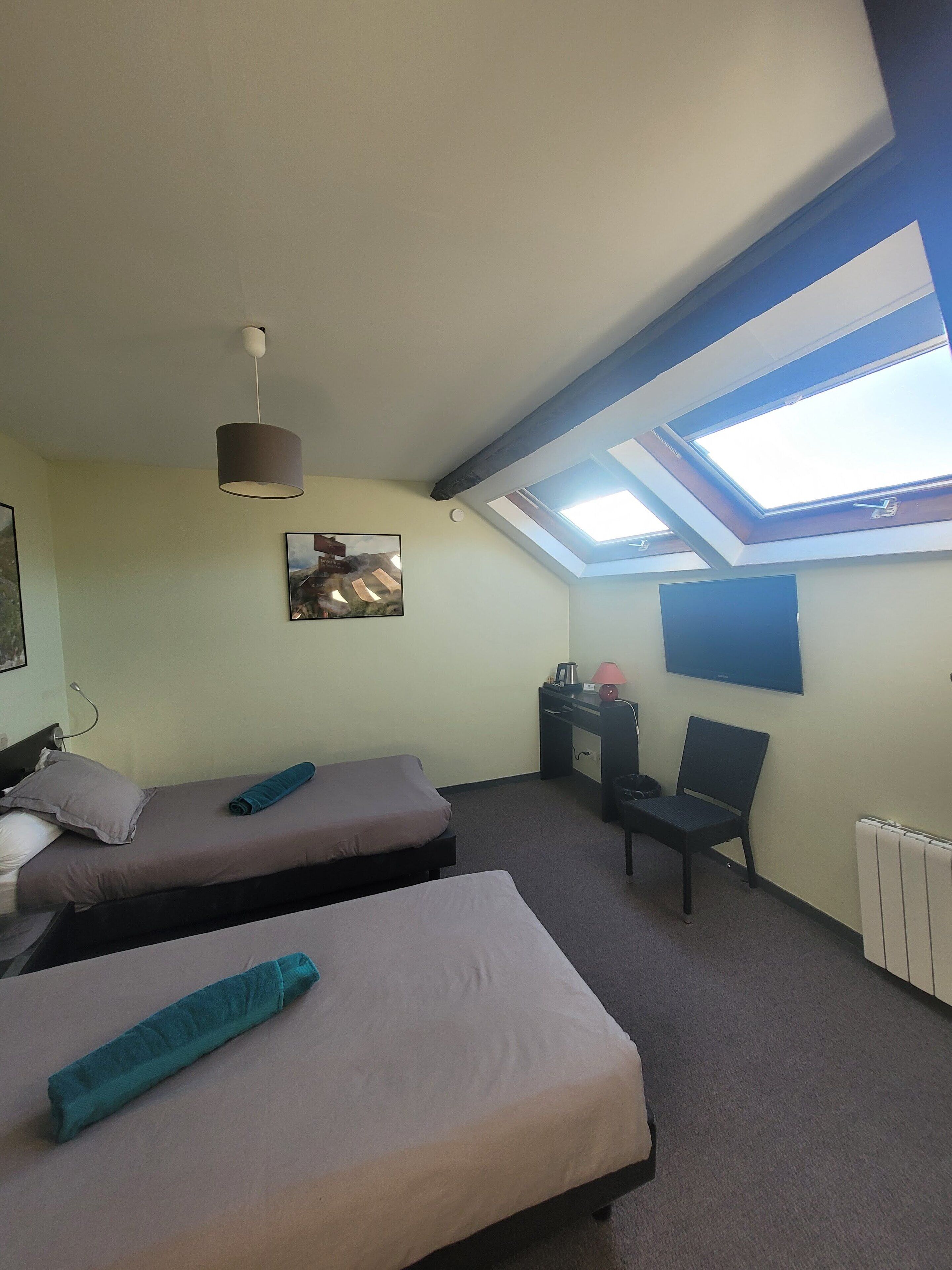A room with two beds, a desk, a chair, a TV, and skylights.