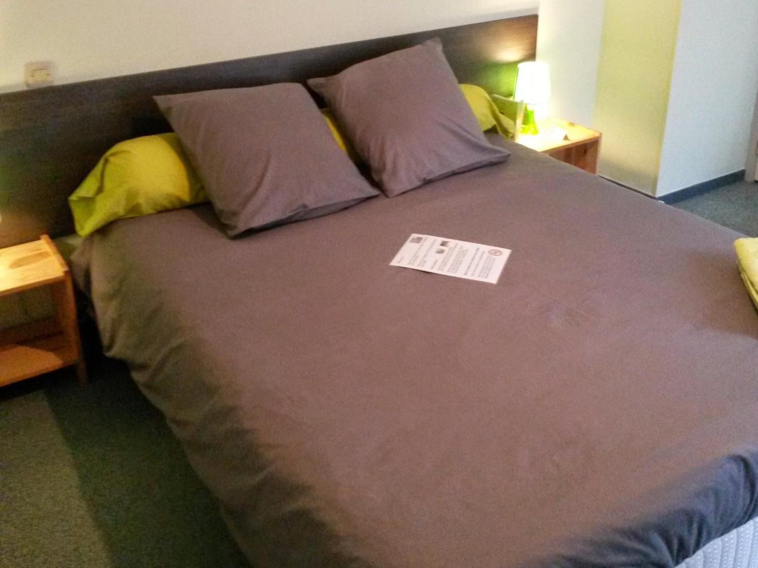 A neatly made bed with a brown bedspread and two pillows, a bedside table with a lamp, and a small nightstand.