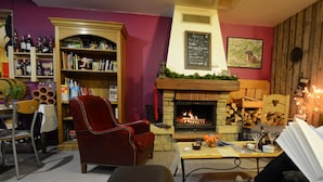 Una sala de estar acogedora con chimenea, estanterías, un sillón rojo y una mesa con bebidas y papeles.