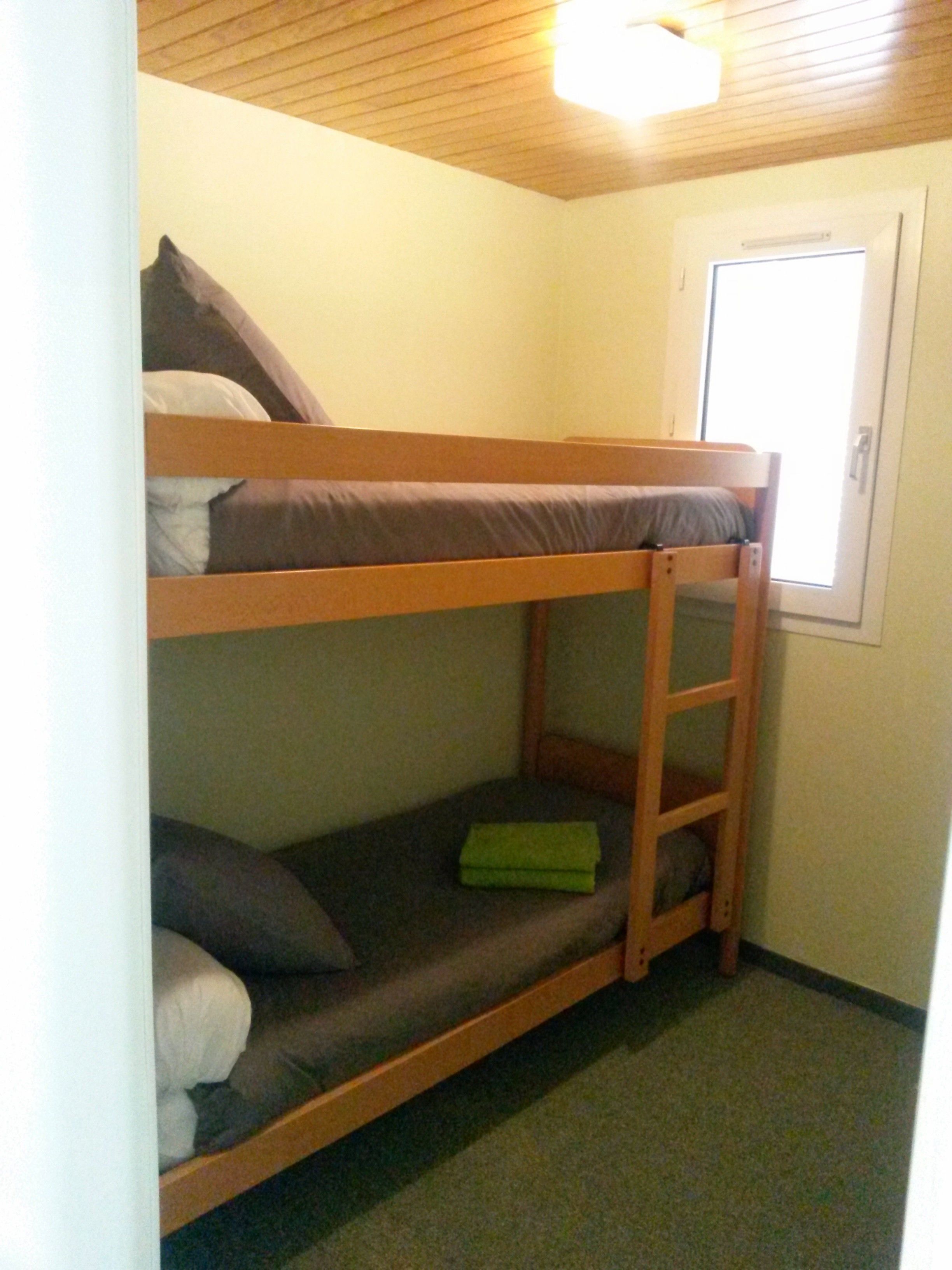 Une chambre avec un lit superposé, une fenêtre et une porte.