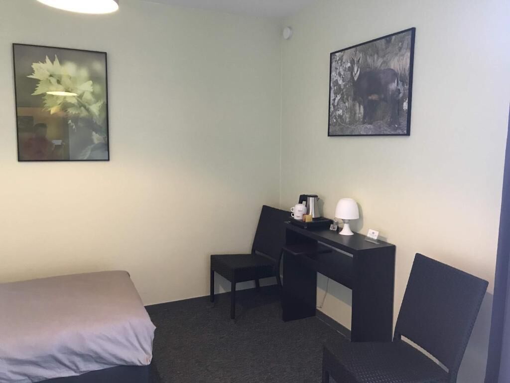Une chambre d’hôtel avec un lit, un bureau avec une chaise, une lampe et deux tableaux encadrés au mur.