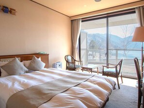 A hotel room with a large bed, two chairs, a desk, and a view of mountains through large windows. - Nikko Chuzenji-ko Onsen Hotel Hana-An (Nikko)