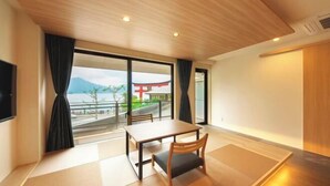 Ein modernes Hotelzimmer mit Holzboden, einem großen Fenster mit Vorhängen, einem Esstisch und einem Fernseher.