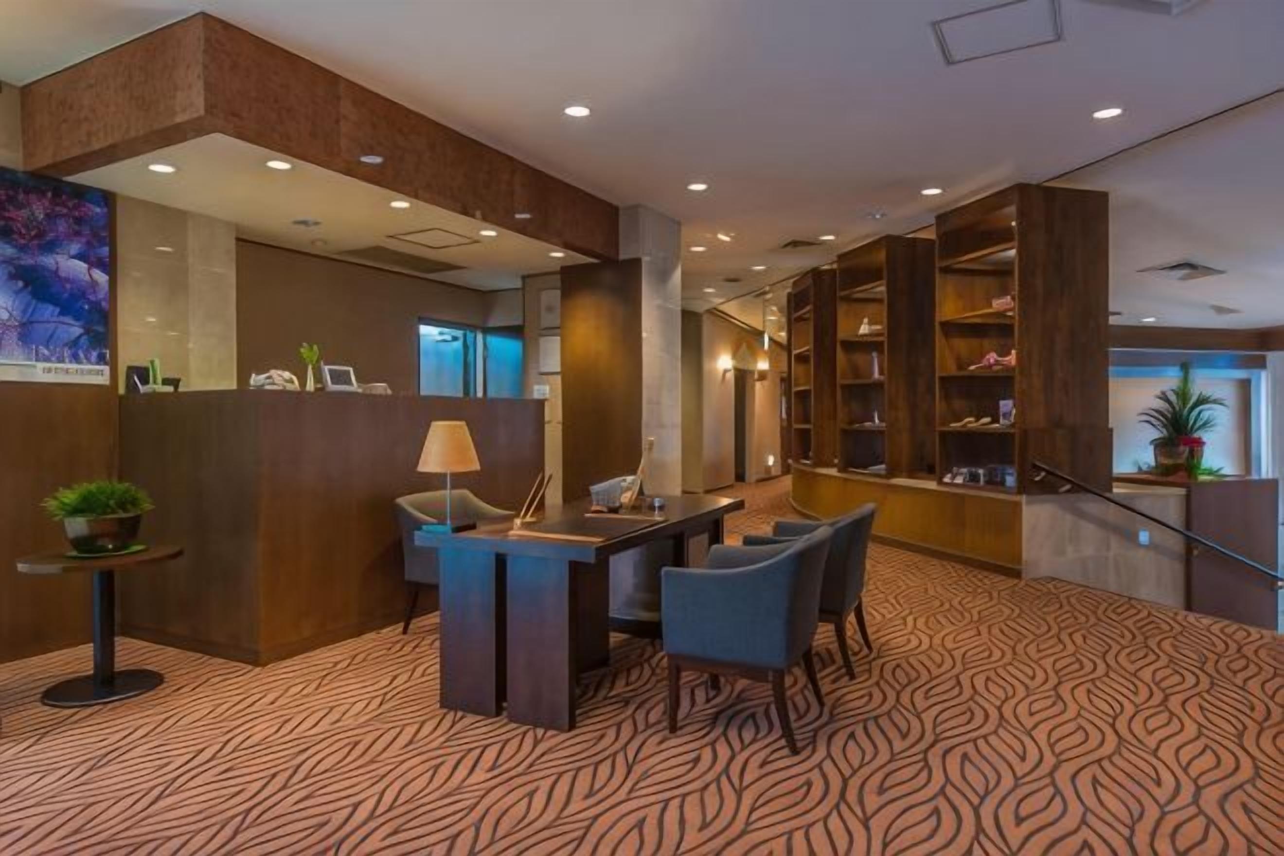 A hotel lobby with a reception desk, seating area, and a staircase leading to an upper level.
