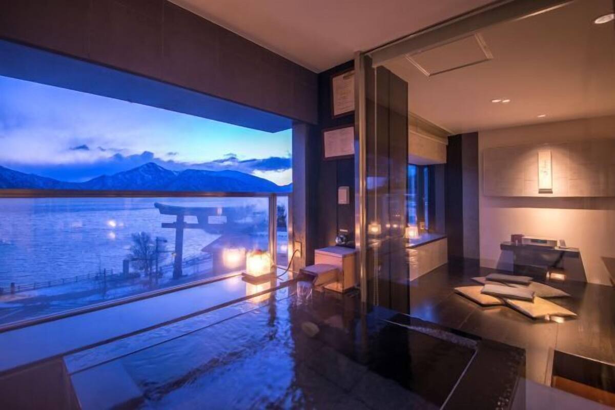 A modern hotel room with a large window overlooking a body of water and mountains.