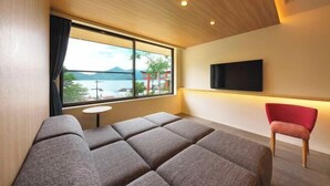Ein modernes Hotelzimmer mit großem Fenster, das Blick auf das Meer und die Berge bietet, einem flachbildfernseher an der Wand und einer gemütlichen Sitzecke mit einem roten Sessel.