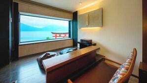 A modern room with a large window offering a view of a body of water and mountains. There is a wooden desk and a bench with a patterned cushion.