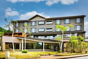 Een meerhoog hotel met een overdekte ingang, een aangelegde tuin en een heldere lucht.