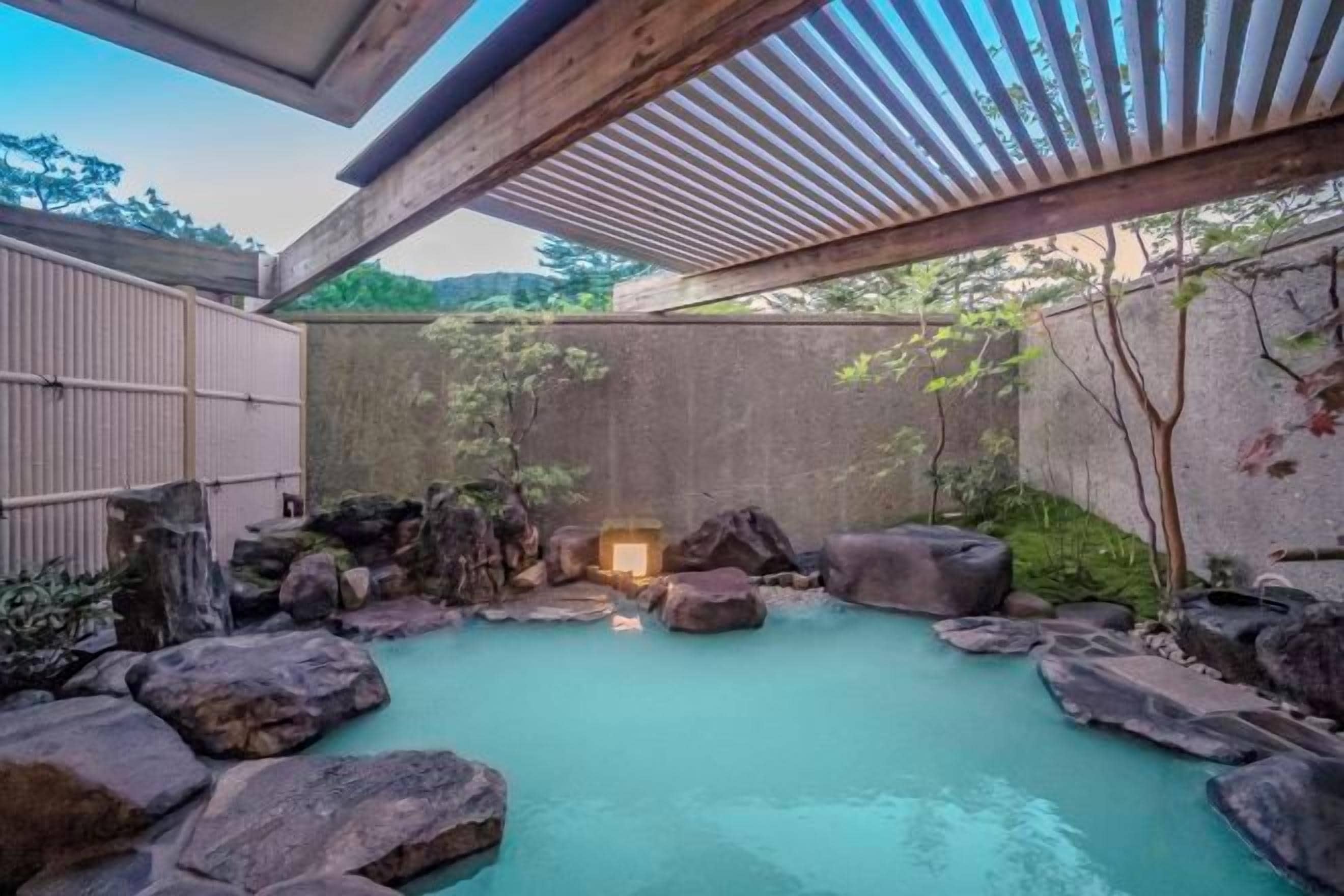 A traditional Japanese onsen with a stone bath surrounded by rocks and a wooden structure overhead.