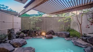 A traditional Japanese onsen with a stone bath surrounded by rocks and a wooden structure overhead.