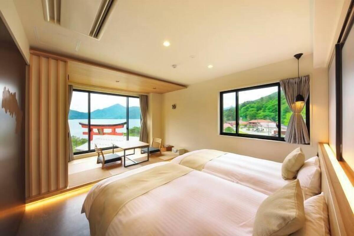 A hotel room with a large bed, a desk, and a view of a traditional Japanese torii gate and mountains.