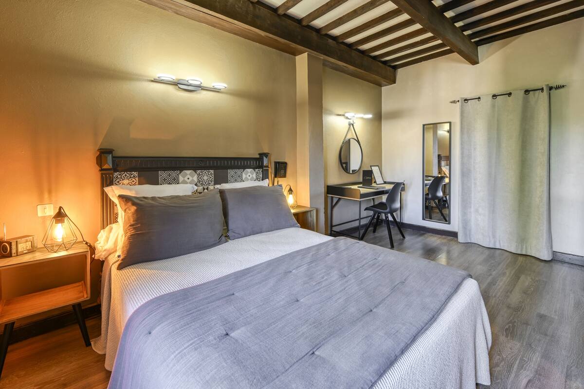 A bedroom with a large bed, bedside tables, a desk, and a mirror.