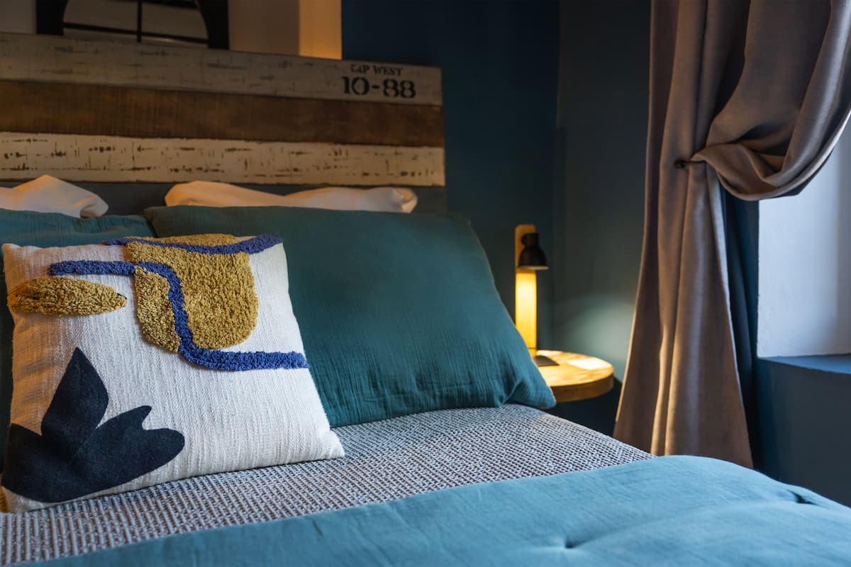 A neatly made bed with a patterned pillow, a headboard with a rustic design, and a lamp on a bedside table.