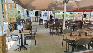 An outdoor café with wooden tables and chairs, covered by a canopy.