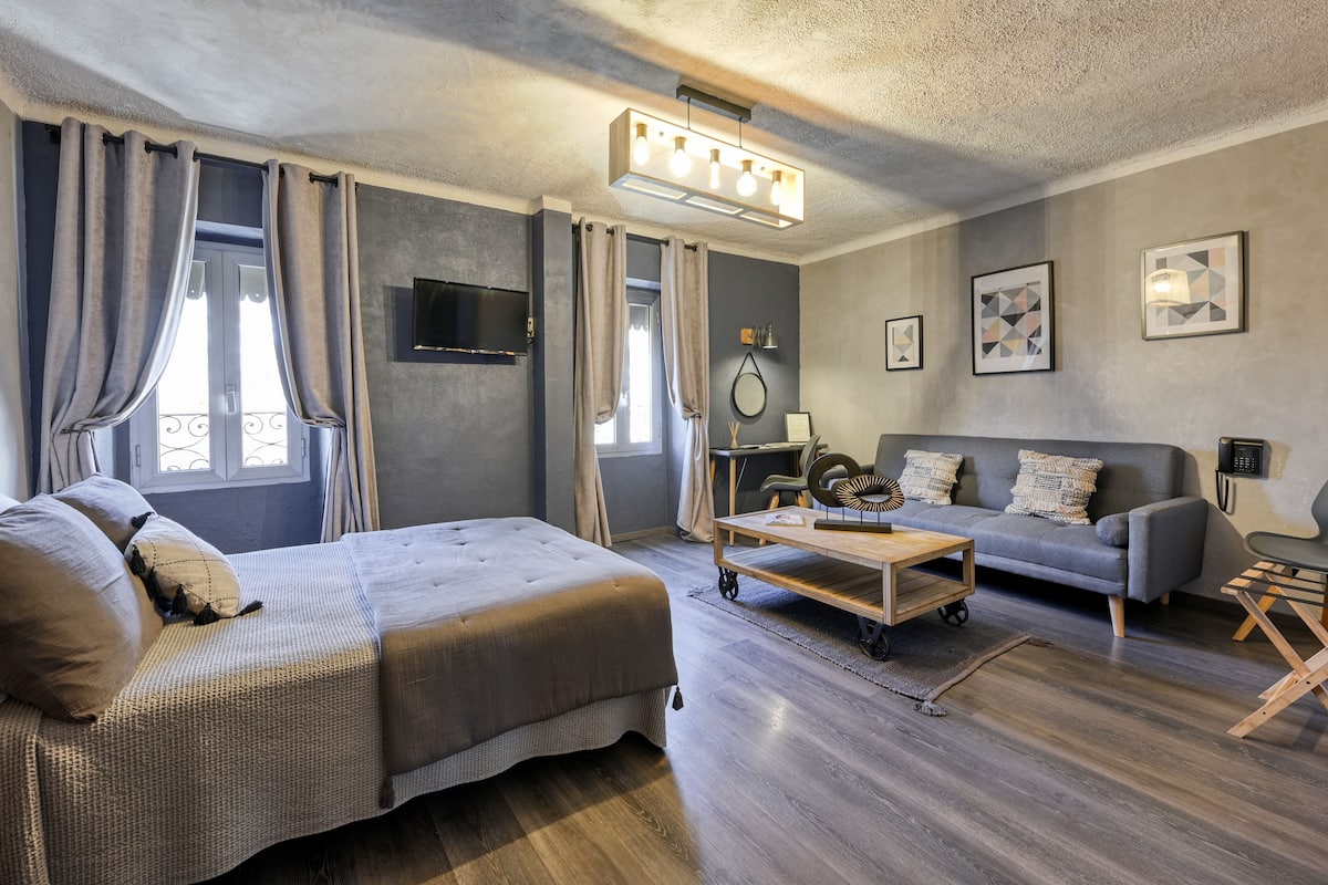 A modern bedroom with a large bed, a sofa, a desk, and a ceiling light fixture.