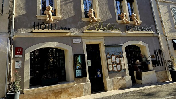 Un edificio con cartel de hotel y restaurante. Se ven ventanas con osos de peluche en el alféizar.