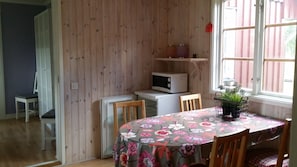 A dining area with a table covered in a floral tablecloth, wooden chairs, a microwave, and a small refrigerator. - Knut's Camping och Lägenheter (Torsby)