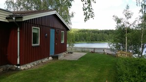 Une cabane rouge avec une porte bleue, un petit porche et une vue sur un lac entouré d’arbres.