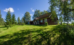 Een houten huis met een veranda, omgeven door een gazon en bomen.
