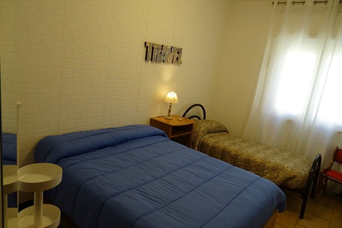 Una habitación con dos camas, una mesita con una lámpara, una silla y una pared decorada.