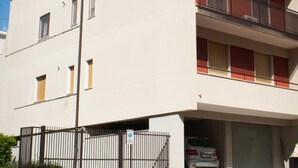 Un immeuble de deux étages avec une façade plate, un balcon à l’étage supérieur et une voiture garée dans le garage.