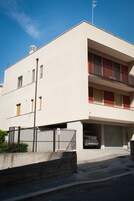 Un edificio di due piani con facciata piatta, un balcone al piano superiore e un'auto parcheggiata nel garage.