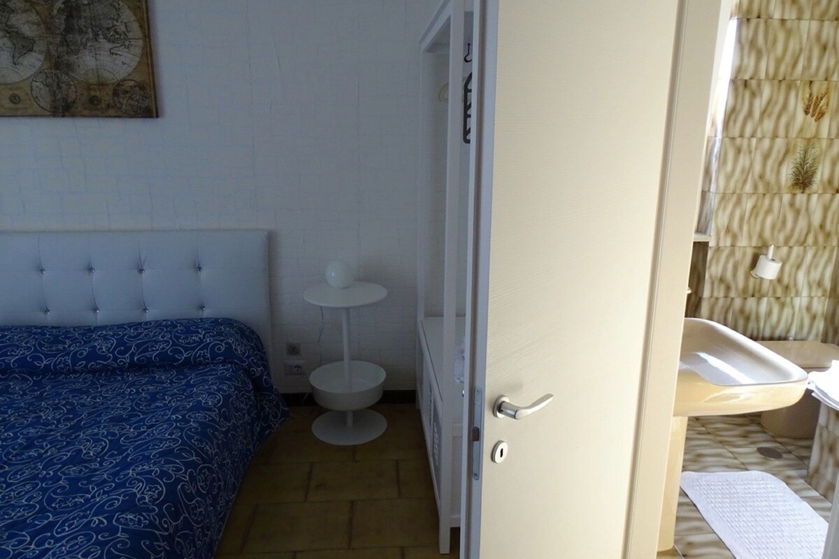 A bedroom with a bed, a small white table, and a door leading to a bathroom.