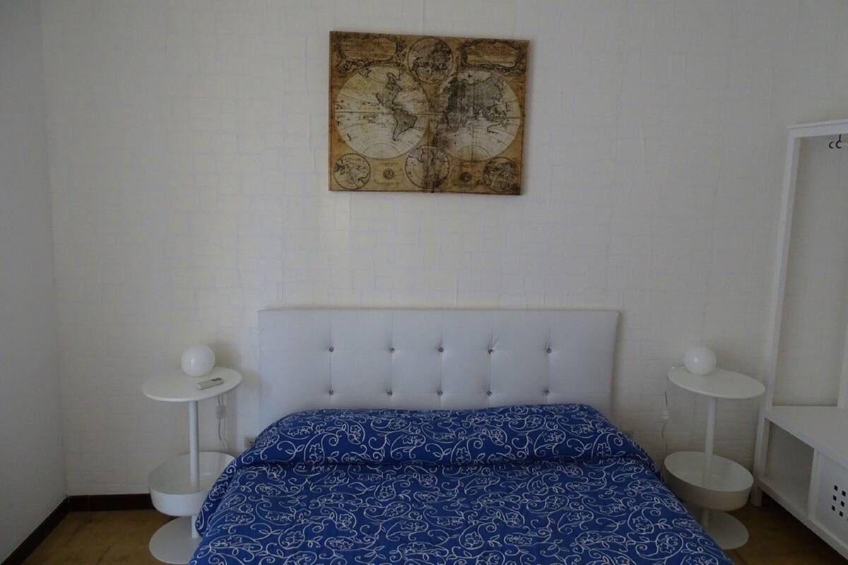 Un dormitorio con cabecera blanca, colcha azul estampada y un mapa grande en la pared.