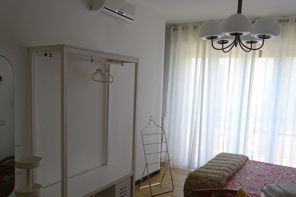 A bedroom with a bed, a wardrobe, a drying rack, and a chandelier.