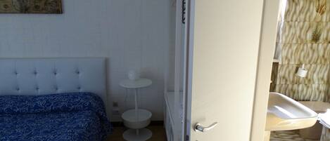 A bedroom with a bed, a small white table, and a door leading to a bathroom.