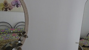 Une vue en miroir d’une pièce avec un lit, une chaise et un mur orné d’un motif floral.