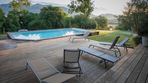 Um deck de madeira com piscina, espreguiçadeiras e vista para montanhas.