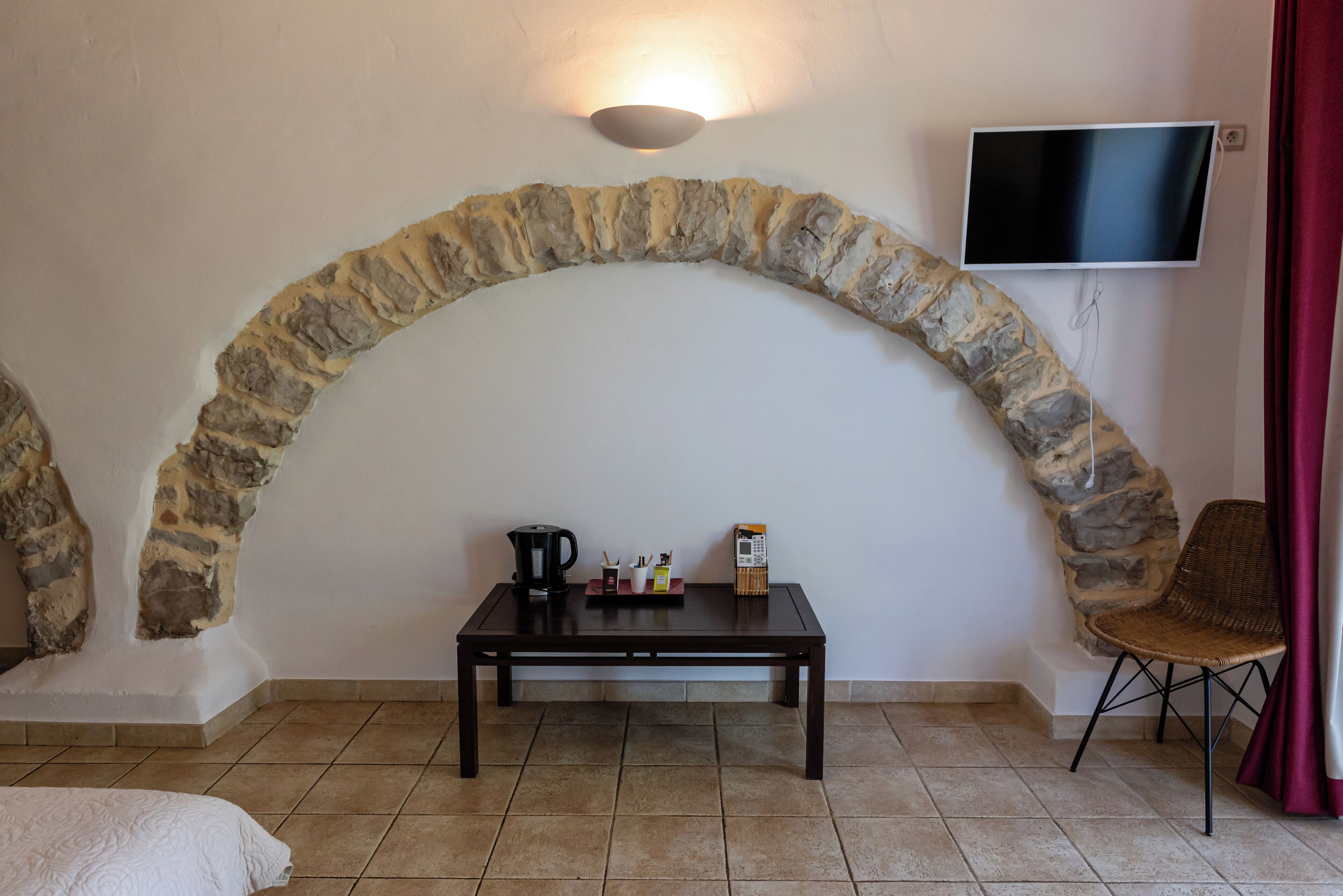 Ein Zimmer mit einer Wand aus Stein, einem flachbildfernseher an der Wand, einem kleinen Tisch mit Kaffeekocher, Tassen und einer Taschentuchbox.