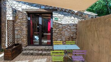 A stone building with a tiled roof, a wooden bench, and a table with colorful chairs.