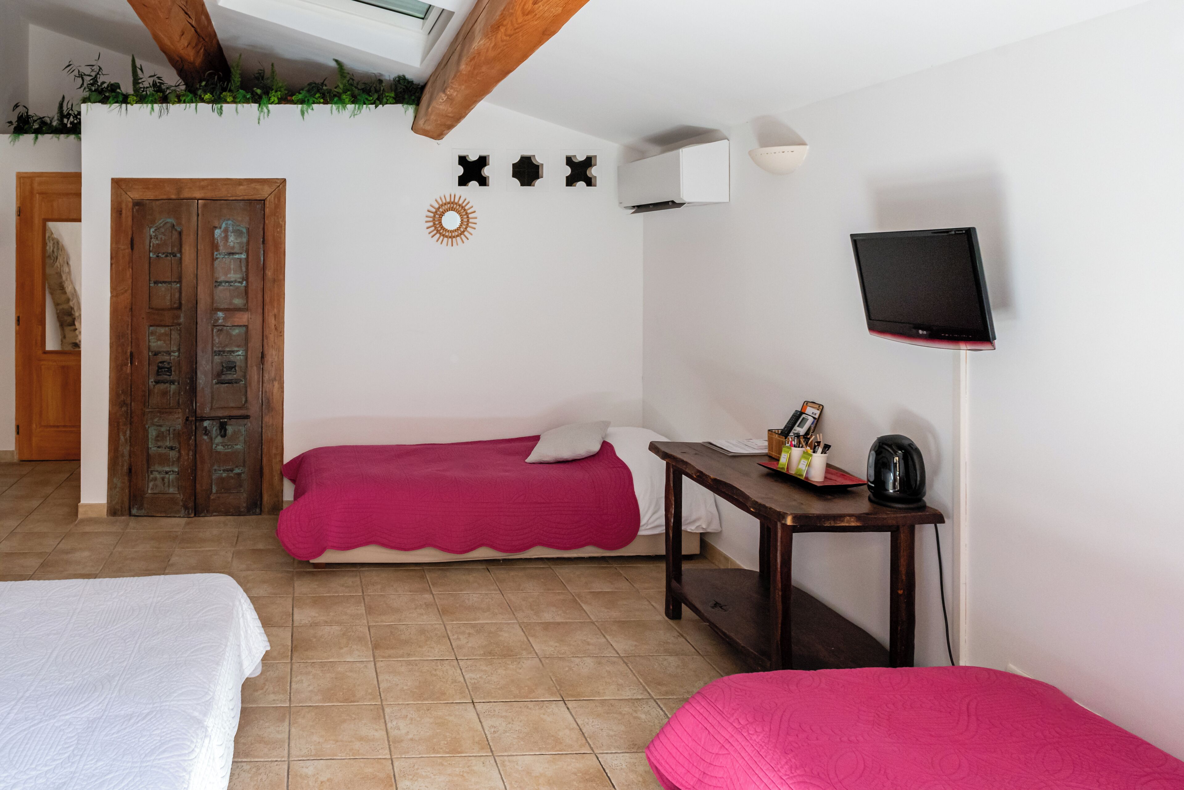 Une chambre avec deux lits, une porte en bois, une petite table avec une bouilloire et un téléviseur fixé au mur.
