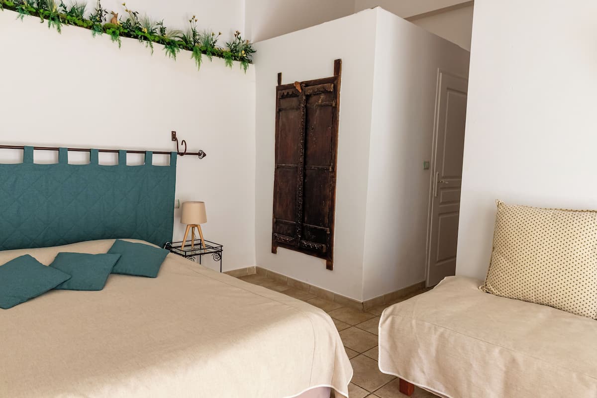 A bedroom with two beds, a wooden wardrobe, a small bedside table with a lamp, and a decorative wall hanging.