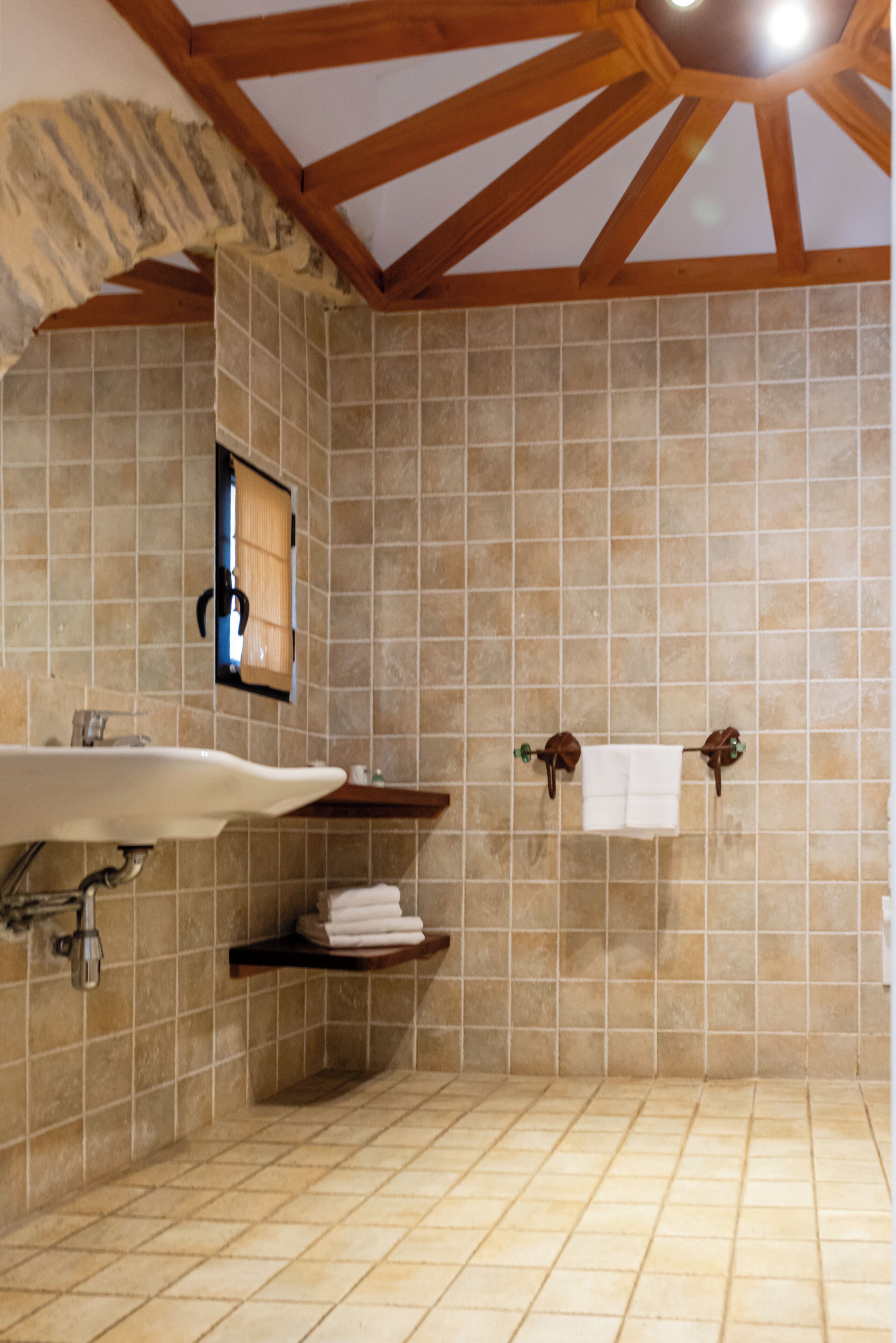 Un bany amb sòl de rajola, un lavabo, sostre de fusta i un suport per a tovalloles.